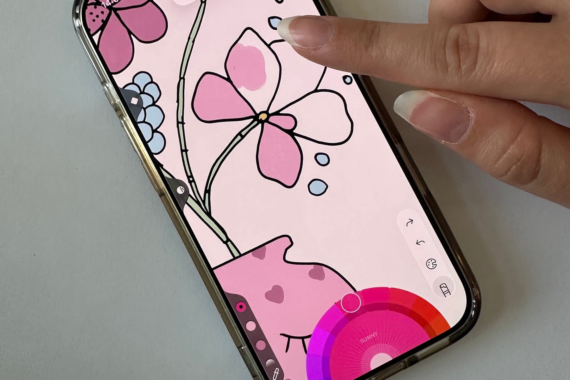 A close-up of a person using their finger to color a digital drawing on an iPhone screen, with bright colors filling in a design directly through touch interaction.